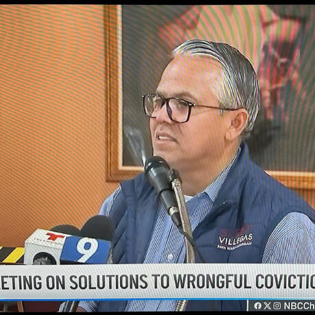 a man in glasses sitting at a podium with microphones