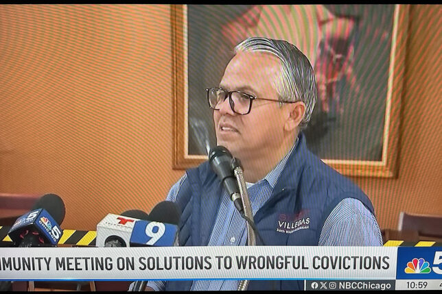 a man in glasses sitting at a podium with microphones