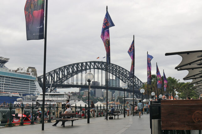 a bridge with flags and people walking on benches