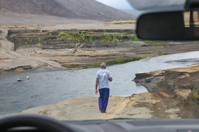 a man walking on a dirt road near water