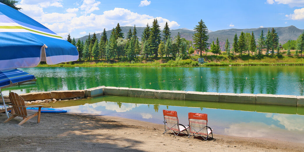 a lake with chairs and a blue umbrella