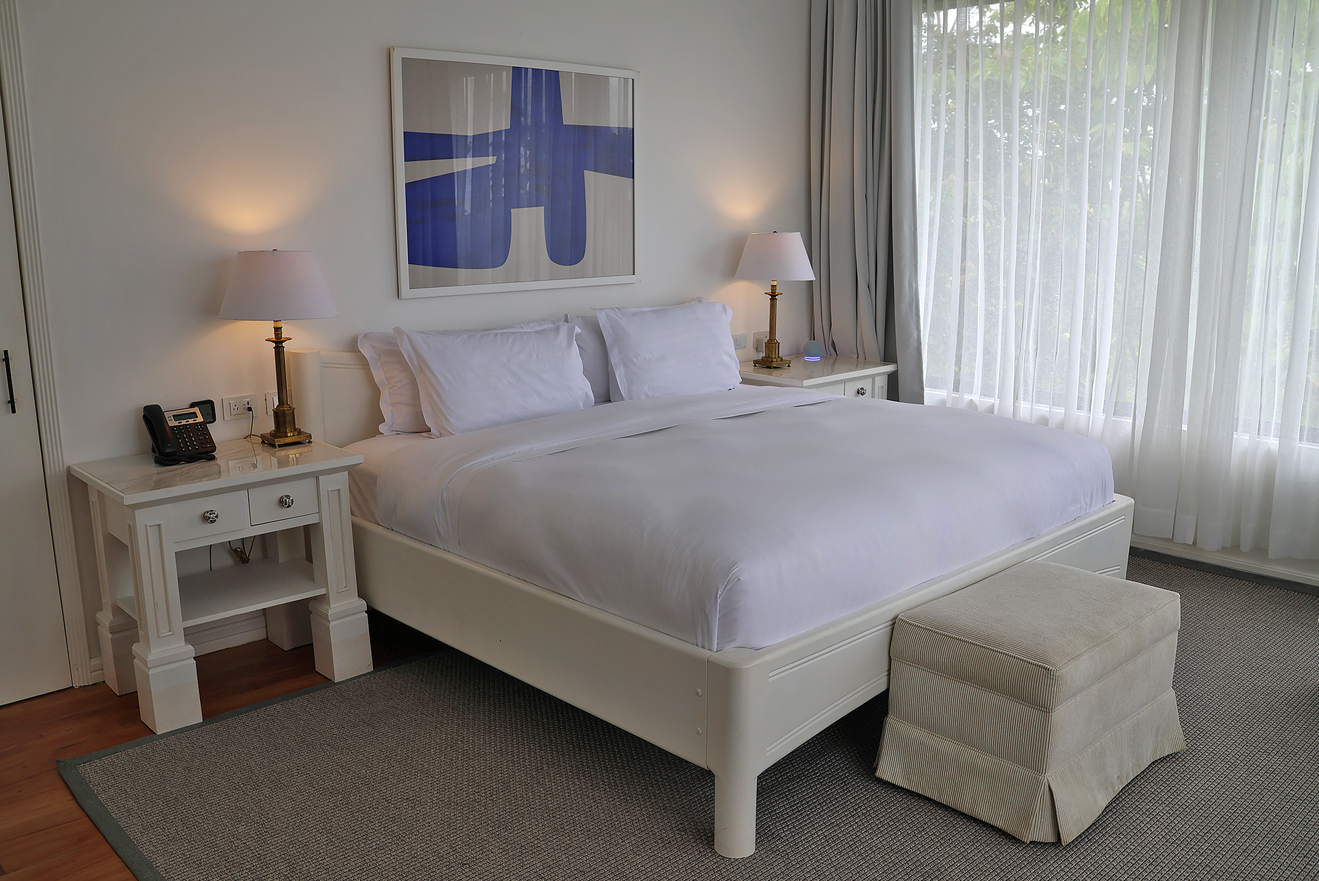 a bed with white sheets and pillows in a room with a painting on the wall