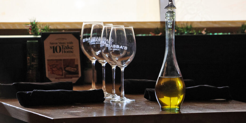 a glass bottle with a yellow liquid next to several wine glasses