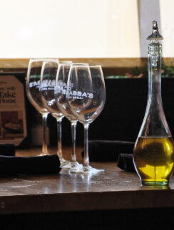 a glass bottle with a yellow liquid next to several wine glasses