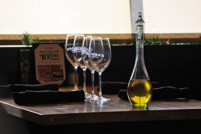 a glass bottle with a yellow liquid next to several wine glasses